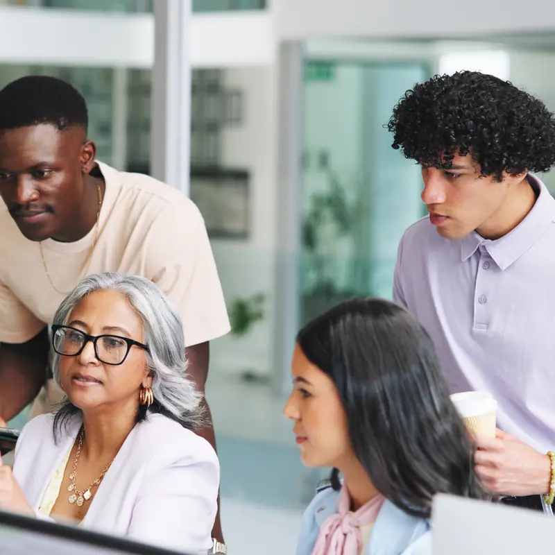 Four colleagues of different backgrounds gathered around a computer screen in a bright office